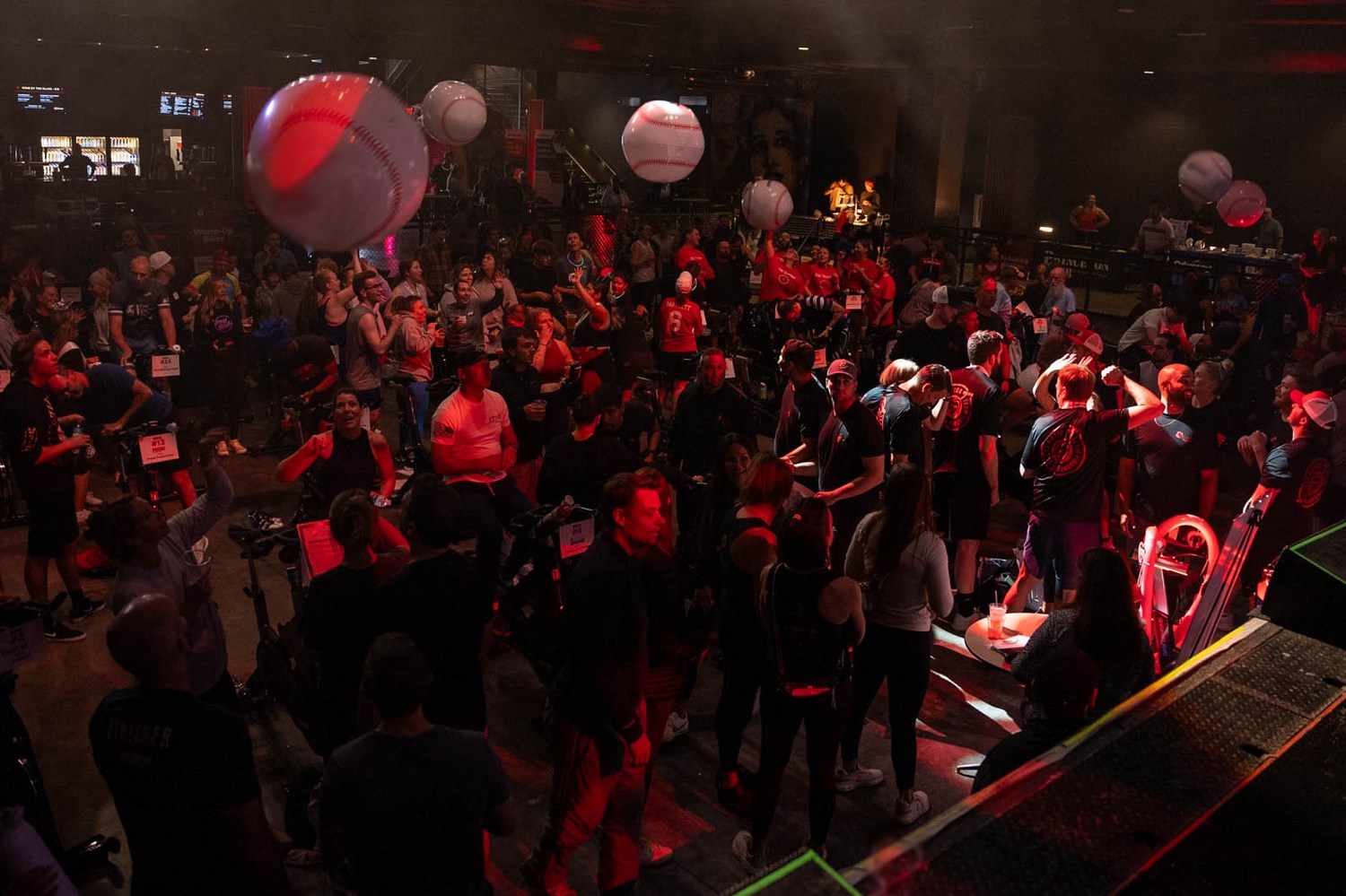 Image of room with lots of people having fun and tossing beach balls in the air that look like baseballs