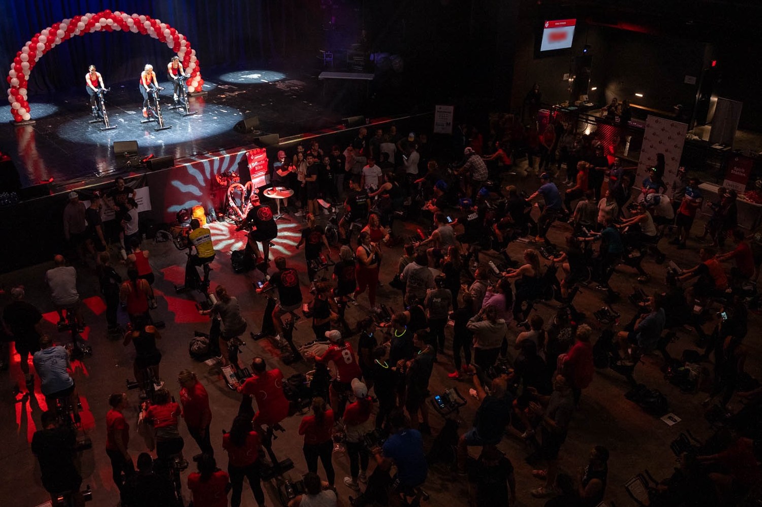 Image of room with lots of teams near stationary bikes and 3 instructors on stage