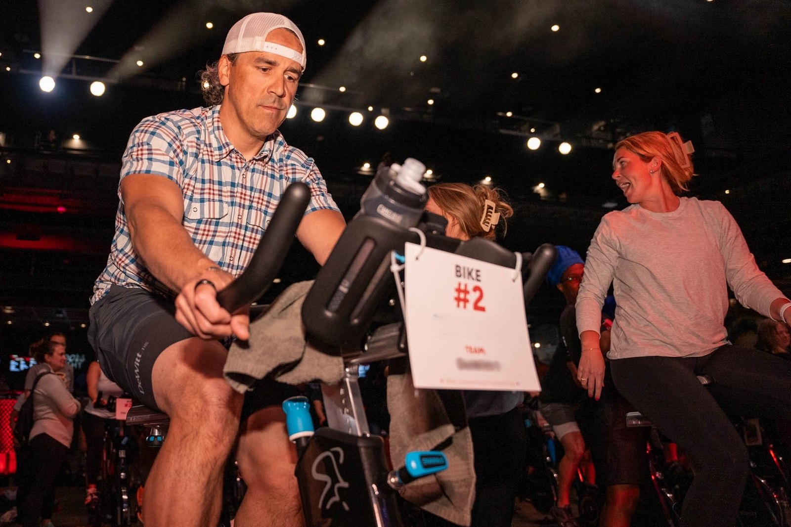 Man in foreground on stationary bike with other riders around talking