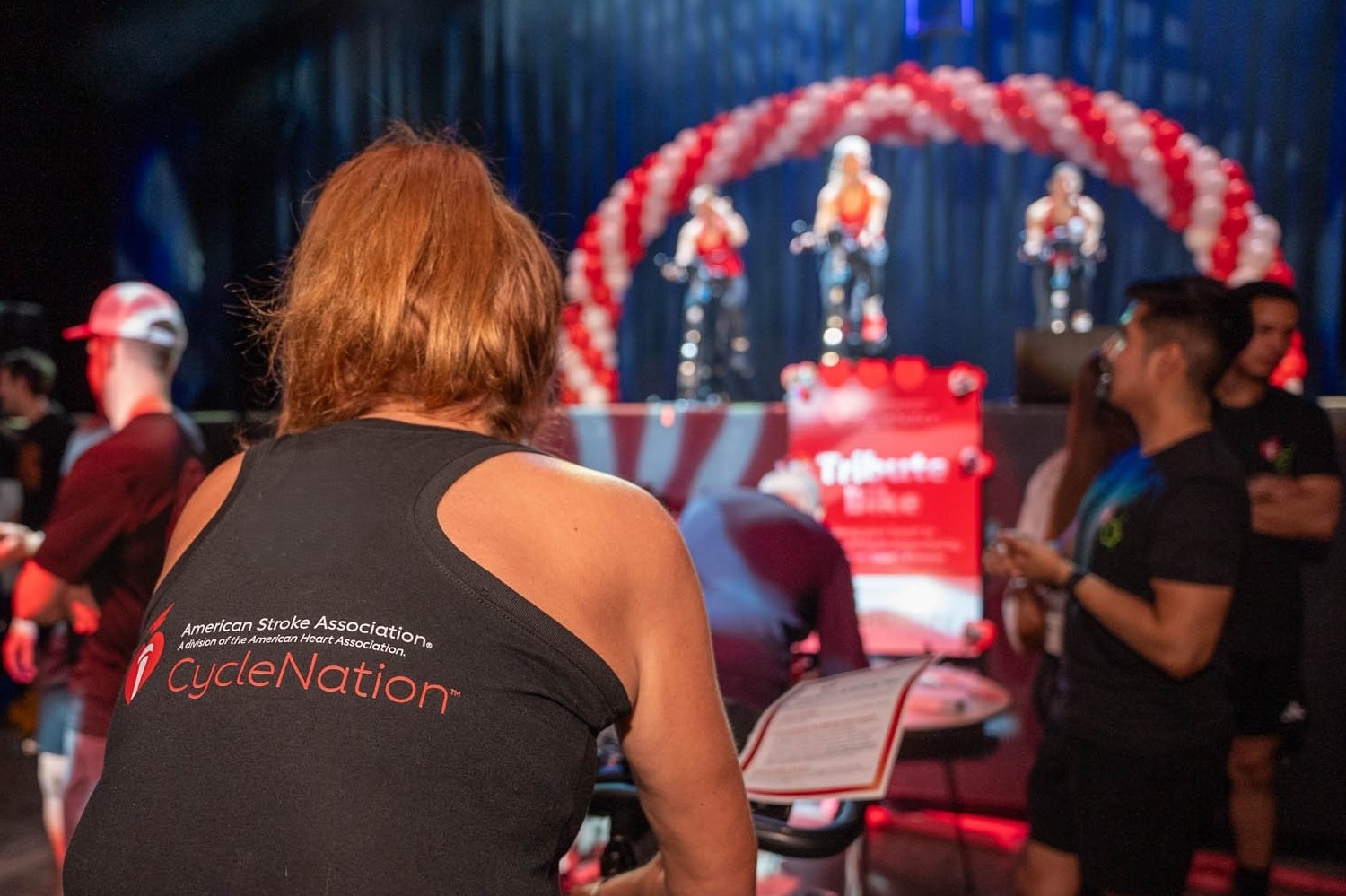 
woman riding a stationary bike with the CycleNation logo on the back of her shirt