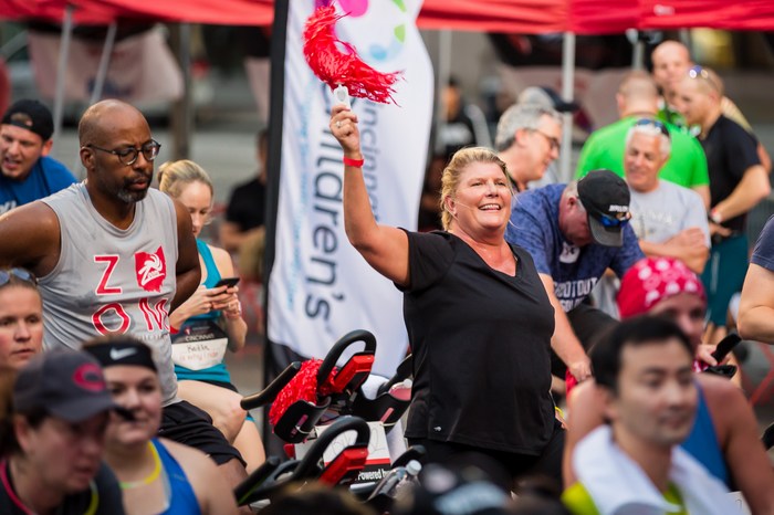 Crowd of stationary bikes with riders - featuring a lady cheering wiht a pompom